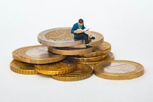 Auf dem Bild sieht man gestapelte Euro Münzen, auf dem eine kleine Figur sitzt. Dies soll die Wirtschaft eines Landes darstellen. Samir Jajjawi erklärt wie eine Firma agiler und flexibler agieren kann.